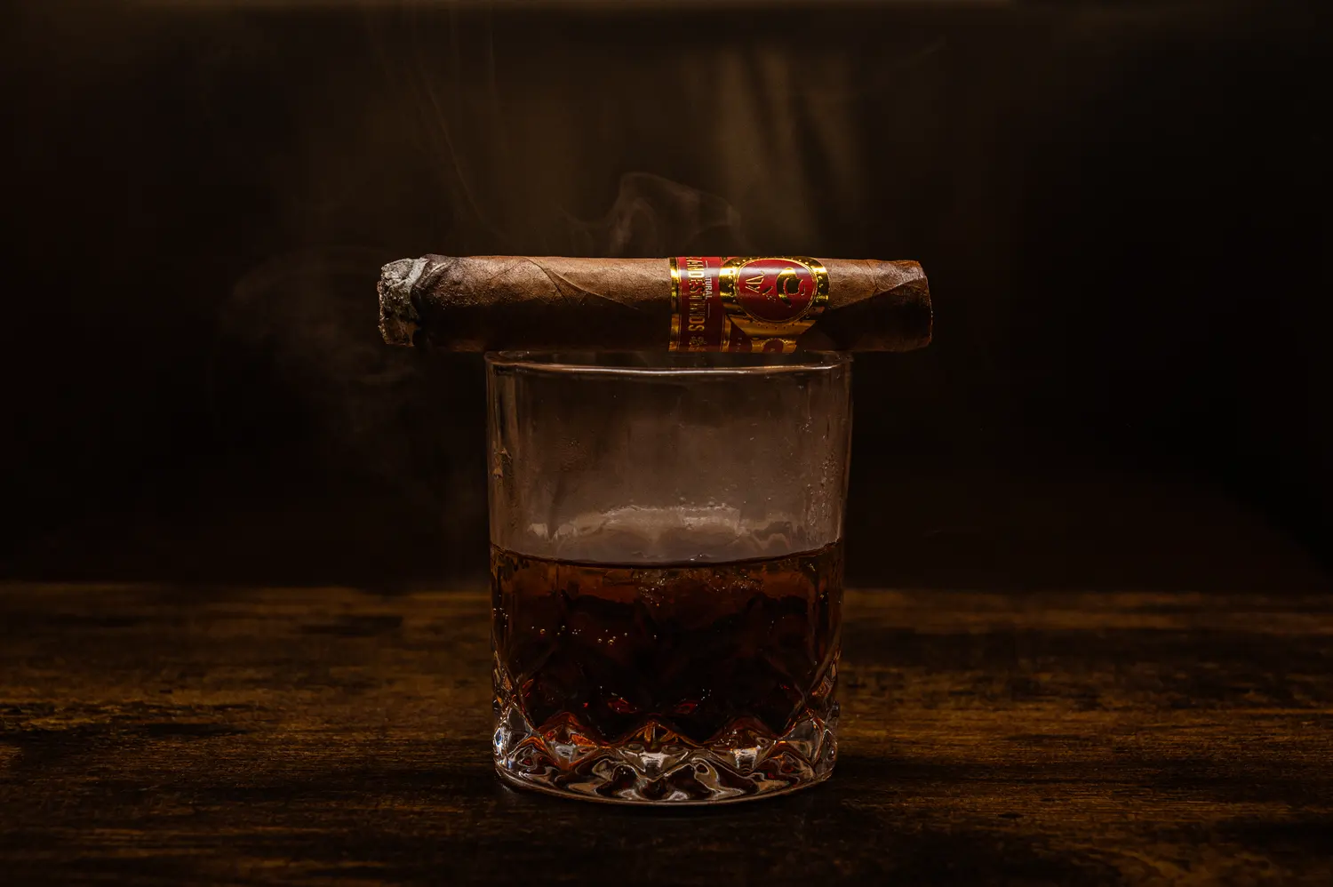 A cigar with a red band resting on a glass of whiskey