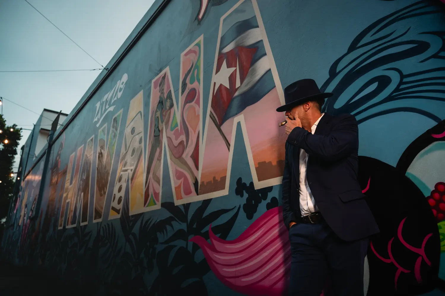 A man in a hat smoking in front of the Little Havana mural
