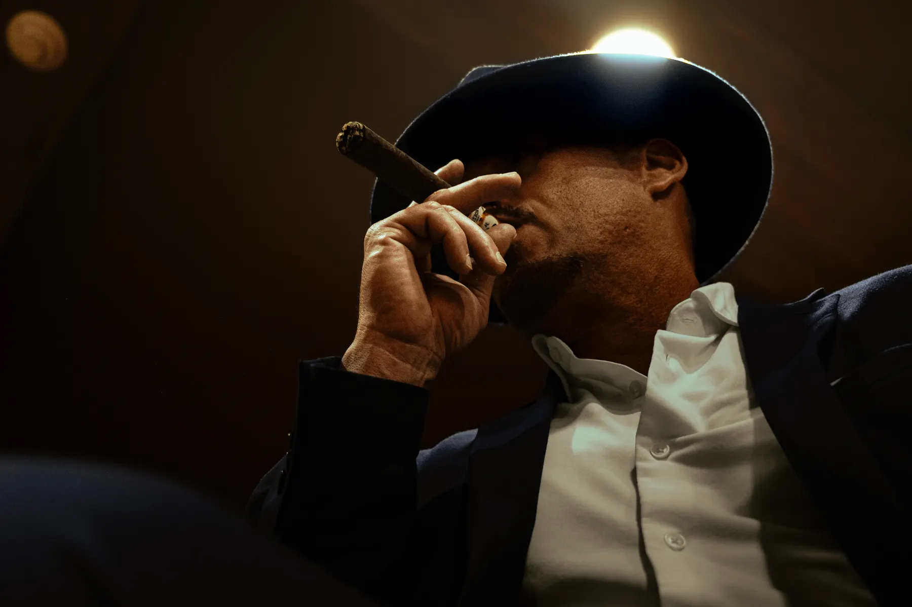 Un hombre con sombrero llevándose un puro a los labios, fotografiado desde abajo